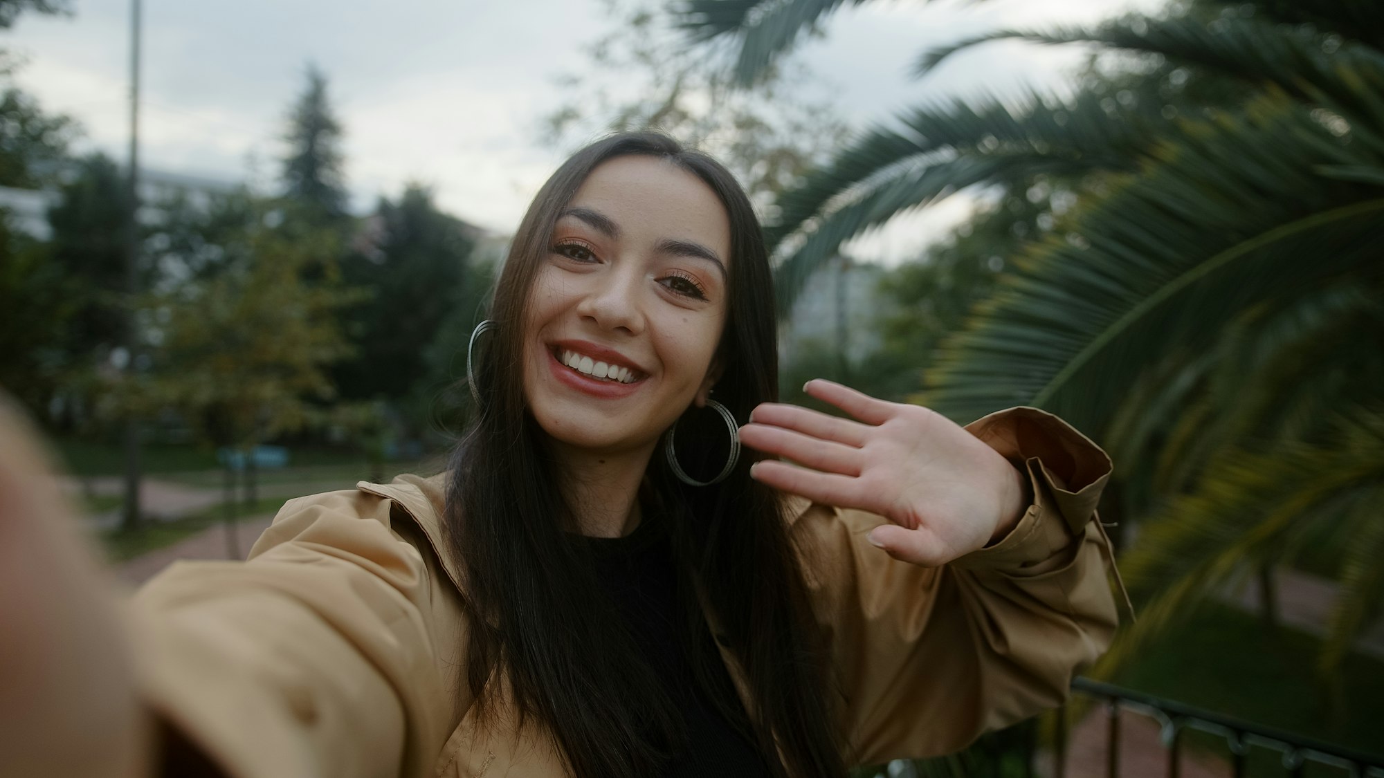 Pretty smiling face woman, holding camera or phone in hand and she is waving to the camera